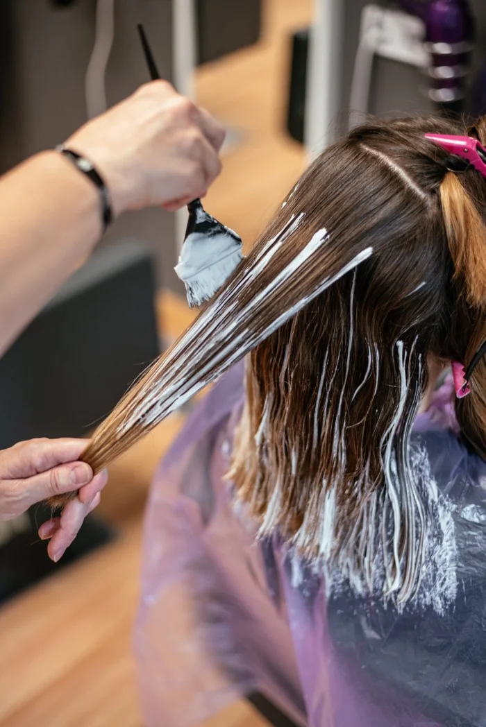 Stylist applying lightener with a brush to create hair highlights on a client at RH Beauty Lounge in Las Vegas